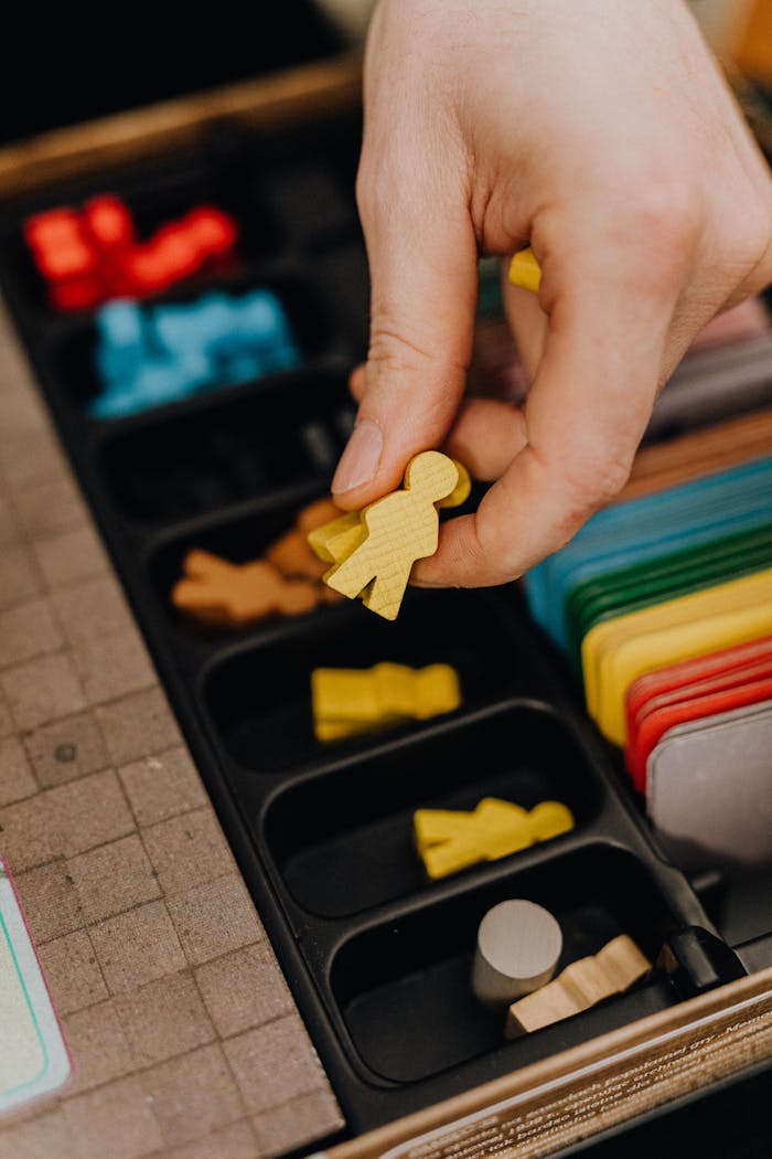 Close-up of a hand arranging colorful board game components, focusing on a yellow piece.